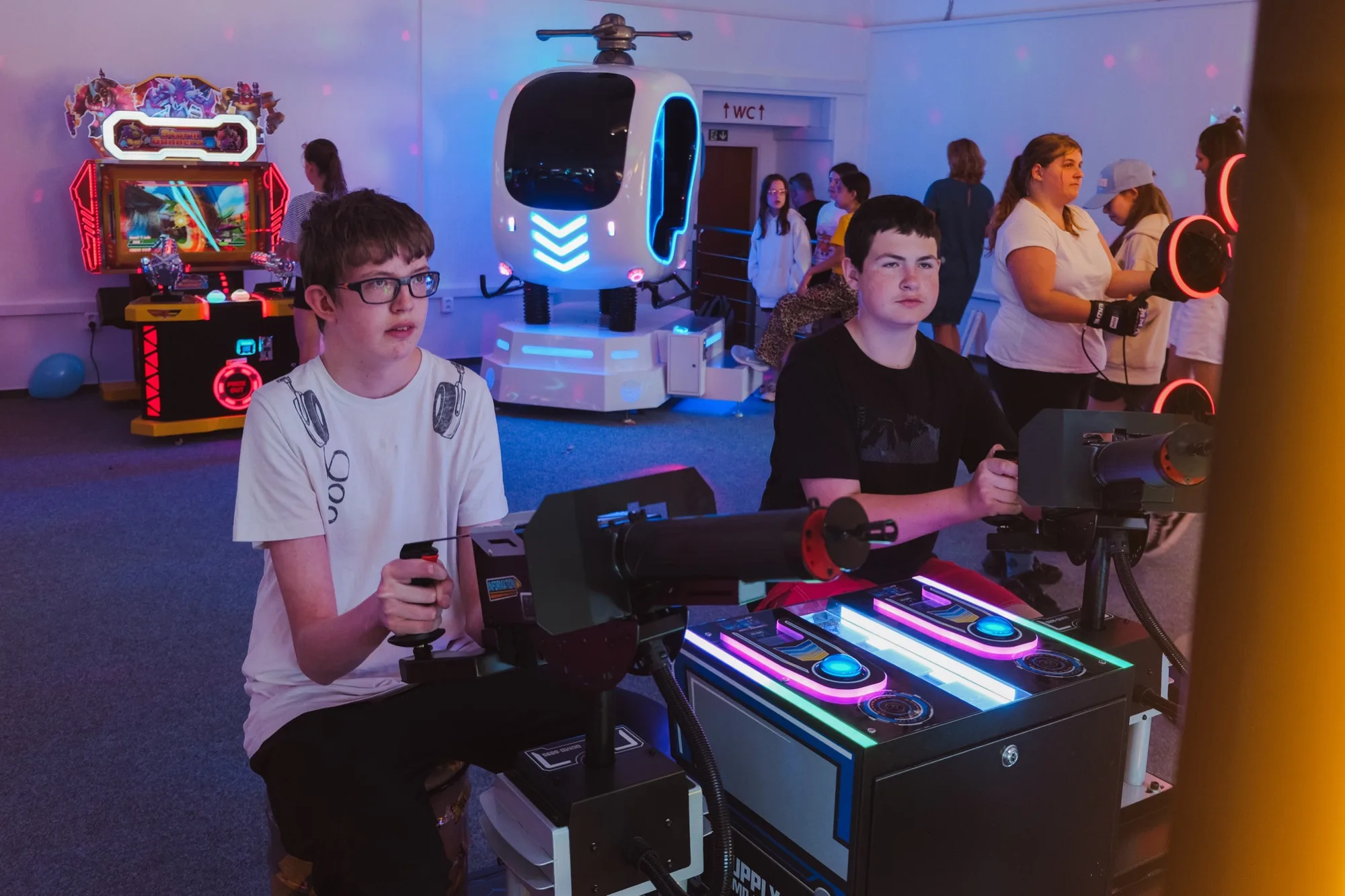 Dva kluci u herního automatu, v pozadí VR simulátor a další atrakce