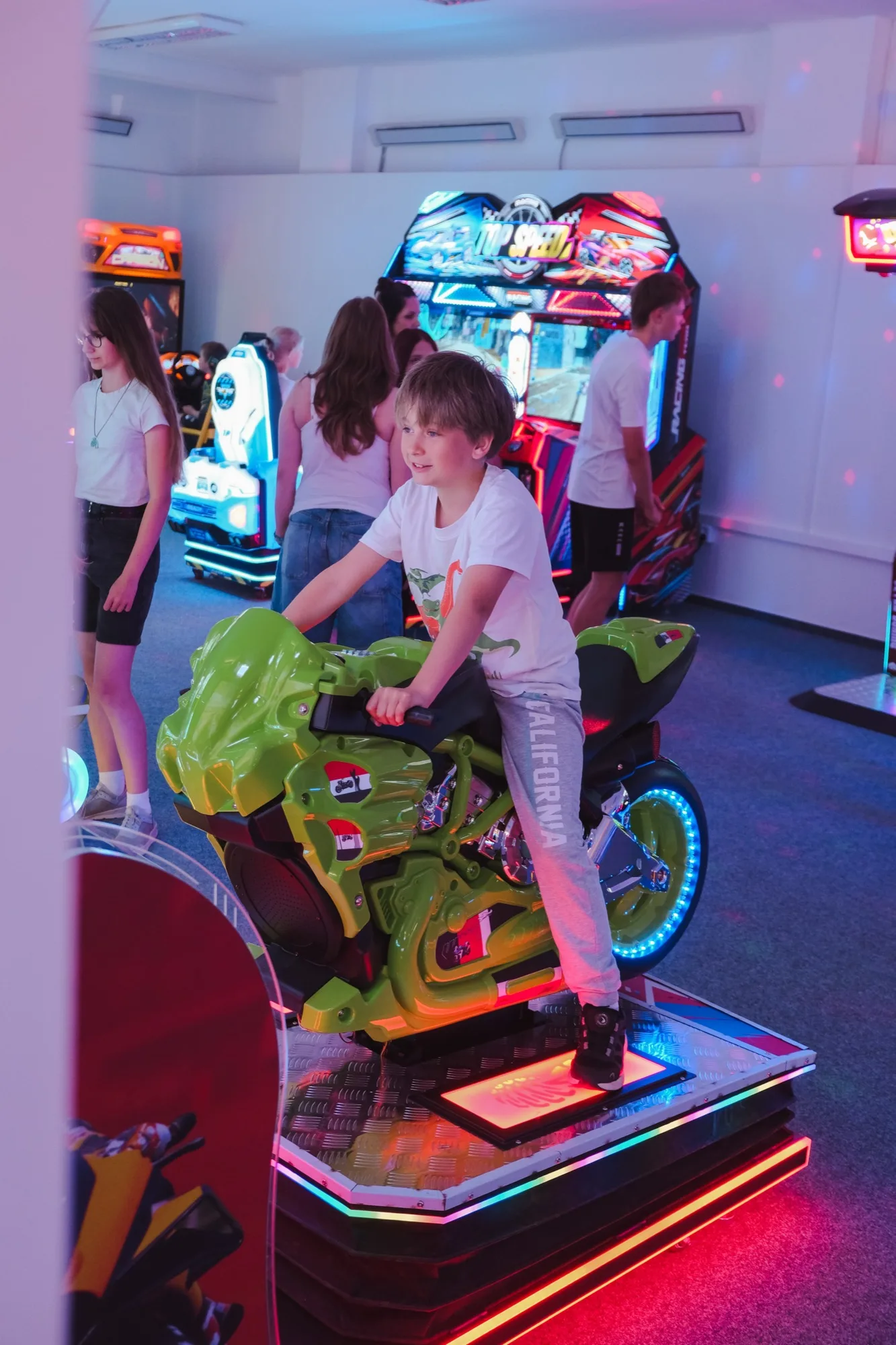 Chlapec na motorkovém simulátoru uprostřed rozsvícené herny Gamecentrum